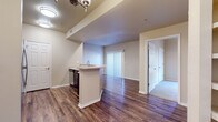 This single-story unit is designed with an open, functional layout that connects the kitchen and living areas seamlessly. The kitchen serves as a central hub, featuring a peninsula with a built-in sink, stainless steel appliances including a refrigerator, range, and microwave, dark espresso cabinetry with tile backsplash, and durable wood-look flooring that extends throughout the main living spaces. A chandelier-style light fixture and recessed lighting provide ample illumination in this area.

The open living space flows naturally from the kitchen toward a windowed wall fitted with vertical blinds, allowing natural light to fill the interior. Built-in shelving adds a practical architectural detail near the transition between rooms.

The bedrooms are finished with plush carpeting and each includes a ceiling fan, windows with horizontal blinds for natural light and privacy, and closet access. The rooms offer a comfortable, well-proportioned sense of space.

Two bathrooms are present in the unit, each sharing a consistent design aesthetic with dark espresso vanity cabinetry, light countertops, large mirrors, brushed nickel fixtures, and wood-look flooring. The overall ambiance of the unit is clean, neutral, and move-in ready.