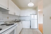 Located at 2440 Hurontario Street in Mississauga, Ontario, this single-floor unit offers a well-organized layout that combines the living room and kitchen into one efficient, open-concept space. The living area is immediately welcoming, finished with warm, polished parquet wood flooring in a classic basket-weave pattern that extends throughout the main living space. Clean white walls and smooth ceilings enhance the sense of brightness and openness throughout.

A standout feature of the living room is the large sliding glass door that opens directly onto a private balcony, allowing for generous natural light and providing views of the surrounding neighbourhood. A secondary window further supplements the natural light, ensuring the space feels airy and bright throughout the day. Baseboard heating units are positioned along the perimeter walls.

The kitchen is a distinct, self-contained space accessible from the living area. It features white cabinetry, a white electric range, white tile flooring, and white tile backsplash, creating a clean and cohesive look. A pendant light fixture adds a functional and decorative touch above the kitchen area. The unit's entry door is conveniently positioned, offering a clear and practical flow between the entrance, living room, and kitchen. Overall, the unit presents a tidy, functional, and well-lit living environment.