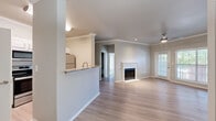 This single-story, 3-bedroom, 2-bathroom home offers a thoughtfully designed open-concept layout finished with light-toned luxury vinyl plank flooring throughout. The combined kitchen and living area serves as the heart of the home, where a peninsula with granite countertops and an undermount sink connects to the kitchen, which is equipped with white cabinetry, stainless steel appliances including a refrigerator, range, and microwave. Crown molding and a ceiling fan add a refined touch to the living room, which is anchored by a classic white-framed fireplace and receives natural light through large windows and a glass-panel exterior door. The three bedrooms are generously proportioned, each featuring windows with blinds that invite natural light, neutral walls, and ceiling fans or light fixtures. Two closets provide dedicated storage. The bathrooms are clean and functional, with one featuring a tub-shower combo, white tile surround, and granite-topped vanity with white cabinetry. A dedicated laundry room houses a full-size washer and dryer. Two hallways connect the spaces efficiently. The overall ambiance is bright, neutral, and move-in ready.