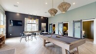 Located at 2626 Goose Island Dr in Leland, NC, this single-story clubhouse blends coastal charm with contemporary design across a thoughtfully arranged layout. Light wood-look tile flooring flows throughout, unifying the various distinct zones within the space.

The main gathering area serves as the social heart of the clubhouse, anchored by a substantial pool table beneath woven rattan pendant lights. Soft sage-green walls contrast with dramatic dark shiplap accent walls, one of which features a mounted flat-screen television above a comfortable lounge seating arrangement. Sliding barn doors along one wall lead to private work pods, while floor-to-ceiling glass partitions enclose additional office or meeting rooms, maintaining an open, airy feel.

A built-in wet bar area showcases decorative tilework in earthy green tones, warm wood cabinetry, pendant sconces, and counter seating, making it an ideal spot for casual gatherings. A separate lounge nook features white shiplap walls, built-in bench seating, and abundant natural light from large windows with outdoor views. Exposed wooden ceiling beams add architectural warmth to the reception area.

Large black-framed glass doors open directly onto a covered outdoor patio, seamlessly connecting the interior with the exterior entertaining space.