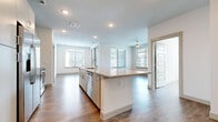 This single-floor residence showcases a clean, contemporary design with a cohesive aesthetic carried throughout each space. The open-concept kitchen serves as the heart of the home, anchored by a generously sized island with granite countertops and an integrated sink. White cabinetry extends to the upper walls, complemented by a white tile backsplash and a full suite of stainless steel appliances, including a French-door refrigerator, range, and built-in microwave. Light wood-style flooring runs continuously across the living areas, enhancing the sense of openness and flow.

The living and dining areas benefit from multiple large windows fitted with horizontal blinds, allowing ample natural light while maintaining privacy. Ceiling fans are present in the main living areas and bedrooms, contributing to both comfort and airflow. A sliding glass door provides access to an outdoor space, further connecting the interior to the outside.

The bedrooms are well-proportioned with large windows and closets featuring five-panel doors. The primary bathroom includes a dual-sink granite vanity with gray cabinetry, a walk-in glass shower, and a soaking tub. A secondary bathroom mirrors the same design language with a granite vanity and convenient access to an adjacent closet.