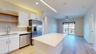Located at 5395 Martway St in Mission, KS, this two-bedroom, two-bathroom residence offers a well-designed single-level layout with a clean, contemporary aesthetic throughout. The open-concept kitchen and living area serve as the heart of the home, where light wood-look flooring, recessed and linear pendant lighting, and a large center island with white quartz countertops set a modern tone. The kitchen is fully equipped with stainless steel appliances—including a French door refrigerator, range, and dishwasher—complemented by white cabinetry with matte black hardware, a subway tile backsplash, and open wood shelving accents. The living area flows naturally toward a wall of windows and a sliding glass door that invites abundant natural light and provides direct outdoor access, enhanced by a ceiling fan overhead. Both bedrooms feature plush carpet flooring, ceiling fans, and generous windows. The spacious primary bedroom connects to a dedicated closet with wire shelving and its own bathroom, which showcases a white vanity with quartz counters, matte black fixtures, and light wood-look tile flooring. The second bathroom mirrors the same refined, minimalist design. Two well-proportioned closets provide ample storage throughout this efficiently designed residence.