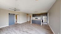 This well-appointed 2-bedroom, 2-bathroom residence in Pittsburgh, PA offers a thoughtfully designed single-level layout with modern finishes throughout. The open-concept living and kitchen area serves as the heart of the home, featuring light wood-look flooring, a ceiling fan, and a striking sliding barn door that adds a contemporary touch. Large windows flood the living space with natural light and frame views of the surrounding neighborhood.

The kitchen is outfitted with dark, rich cabinetry, light quartz countertops, stainless steel appliances including a refrigerator, built-in microwave, and dishwasher, along with a central island that provides additional prep and seating space. A tall window above the counter extends the bright, airy feel.

Both bedrooms are carpeted and receive abundant natural light through well-positioned windows with neighborhood views. The primary bedroom connects to an en-suite bathroom featuring a dual-sink vanity with dark cabinetry, quartz countertops, and wood-look tile flooring. The second bathroom offers a glass-enclosed shower, single-sink vanity, and matching finishes.

A hallway connects the rooms efficiently, lined with louvered double closet doors that provide generous storage. The neutral color palette and consistent modern design language create a cohesive, comfortable ambiance throughout the home.