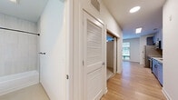 Located at 4200 N Carlin Springs Rd in Arlington, VA, this one-bedroom, one-bathroom unit offers a thoughtfully designed layout across a single floor. The open-concept living and dining area is bright and airy, anchored by light wood-style flooring and a large window that invites natural light and outdoor views, complemented by a ceiling fan overhead. The kitchen is well-appointed with gray flat-front cabinetry featuring black hardware, white quartz countertops, a classic subway tile backsplash, and a full suite of stainless steel appliances including a French door refrigerator, electric range with over-the-range microwave, and a deep single-basin sink with a matte black spring-neck faucet. A hallway lined with louvered doors leads to the bedroom and provides access to in-unit laundry and a dedicated closet. The carpeted bedroom offers a quiet retreat with a ceiling fan, a window for natural light, and a sliding double-door closet for storage. The bathroom is finished with large-format tile surround in the tub/shower combo and matte black fixtures, maintaining a clean, contemporary aesthetic consistent throughout the home.