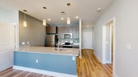 Located at 128 Florence St in Asheville, NC, this single-floor residence offers a thoughtfully designed open layout with modern finishes throughout. The kitchen is a standout feature, showcasing dark espresso cabinetry, granite countertops with subtle veining, a large peninsula with a bold blue accent base, stainless steel appliances including a refrigerator, range, and microwave, and elegant pendant lighting overhead. Light hardwood flooring flows seamlessly through the main living areas and hallways, lending warmth and continuity to the space. The living and dining areas benefit from generous natural light streaming through multiple windows fitted with white blinds. The bedrooms are well-proportioned, with some featuring plush carpeting, ceiling fans, and multiple windows that invite abundant daylight and outdoor views of the surrounding neighborhood. The bathroom is finished with large-format gray tile flooring, dark wood vanity cabinetry, a white countertop, and a tiled tub-shower combination. Neutral, softly toned walls throughout create a calm, cohesive aesthetic that complements the contemporary design elements. The overall layout, as evidenced by the floor plan, provides a functional and comfortable flow between living, dining, kitchen, and private spaces.