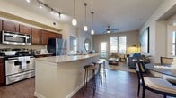 This thoughtfully designed single-story residence offers 1 bedroom and 2 full bathrooms across a comfortable and functional floor plan. The open-concept kitchen and living area serves as the heart of the home, anchored by a large granite-topped island with bar seating and pendant lighting overhead. Rich, dark cabinetry pairs with a full suite of stainless steel appliances, including a refrigerator, range, microwave, and dishwasher, while track lighting illuminates the workspace. Hardwood-style flooring flows seamlessly throughout the main living areas, lending warmth and continuity. The living room is bright and inviting, featuring a ceiling fan, large windows that admit abundant natural light, and direct access to an outdoor area via a glass-panel door. The primary bedroom is a comfortable retreat, finished with plush carpet, a ceiling fan, and a well-sized window with outdoor views. Two bathrooms feature matching dark cabinetry, granite countertops, and wood-style flooring, with one offering a shower-tub combination. A dedicated closet with built-in shelving provides practical storage. The overall ambiance is modern and neutral, with warm tones and clean finishes creating an accessible, move-in-ready living environment.
