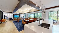 Located at 1350 S Dixie Hwy in Coral Gables, Florida, this thoughtfully designed single-floor amenity space blends contemporary style with functional comfort. Exposed dark wood ceiling beams contrast with crisp white ceilings throughout, creating visual warmth while pendant and drum lighting fixtures provide layered illumination across each zone.

The main gathering area is anchored by a bold blue area rug and features a full-size billiards table alongside a dining table with upholstered chairs, making it ideal for both social events and casual use. Large floor-to-ceiling windows line the perimeter, inviting abundant natural light and offering views of lush greenery outside.

The kitchen area is well-appointed with a generous white quartz island with bar seating, stainless steel appliances including a full-size refrigerator, a mosaic tile backsplash, and rich wood cabinetry. Sleek pendant lights hang above the island, reinforcing the modern aesthetic.

A dedicated workspace area features a built-in desk, a large-screen TV set into a custom dark wood entertainment wall with shelving, and geometric acoustic wall panels. Herringbone-patterned hardwood flooring flows throughout, unifying the space with a refined, cohesive finish.