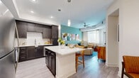 Located in Palmetto, FL, this single-story, one-bedroom, one-bathroom residence offers a thoughtfully designed open-concept floor plan that maximizes functionality and flow. The combined kitchen and living area serves as the heart of the home, where rich dark-espresso cabinetry, a white subway tile backsplash, and stainless steel appliances define a well-appointed kitchen. A central island with a crisp white countertop provides both prep space and casual bar seating, illuminated by elegant pendant lighting overhead. Light wood-tone flooring runs throughout, creating a seamless visual connection between spaces. The living room features a tray ceiling with a ceiling fan, a private exterior door, and large windows that invite natural light, complemented by a striking accent wall. The bedroom is a serene retreat with its own tray ceiling, a ceiling fan, a dedicated closet, and a window with natural light. The hallway connects to a clean, efficiently designed bathroom featuring a glass-enclosed walk-in shower, a pedestal sink, and light, neutral finishes. This residence offers a cohesive, modern aesthetic throughout, combining practical design with inviting details in every room.