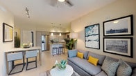 This single-floor residence showcases a thoughtfully designed open-concept layout that seamlessly connects the living, dining, and kitchen areas. The living room is anchored by a comfortable sectional sofa accented with yellow throw pillows, framed wall art, and a ceiling fan overhead. A sliding glass door floods the space with natural light and provides outdoor access. Light-toned tile flooring flows consistently throughout the home, enhancing the sense of openness.

The kitchen is a standout feature, equipped with stainless steel appliances including a French-door refrigerator, electric range, and over-the-range microwave. Flat-front cabinetry in a warm taupe finish pairs with granite countertops, and a central island with bar seating serves as both a prep space and casual gathering spot. Pendant lighting above the island adds a polished finishing touch.

The bedrooms are calm and well-proportioned, each featuring neutral gray walls, natural light from window treatments, and ceiling fans. The primary bedroom offers a sophisticated atmosphere with an upholstered headboard and coordinated décor. Two bathrooms serve the home — one featuring a glass-enclosed walk-in shower, and the other a full tub-shower combination with large-format tile surround and granite vanity countertops.