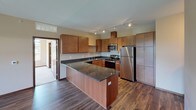 This thoughtfully designed single-floor residence blends modern finishes with a comfortable, functional layout. The kitchen serves as a standout feature, showcasing rich wood cabinetry, dark granite countertops, a peninsula for additional prep and seating space, and a full suite of stainless steel appliances including a refrigerator, range, microwave, and dishwasher. Track lighting illuminates the space, while durable hardwood-style flooring ties the kitchen and living areas together seamlessly.

The living area extends from the kitchen and opens toward a balcony through a glass door, allowing an abundance of natural light to fill the space. Exposed ductwork adds an industrial loft-inspired character, complementing the soaring ceiling height in this area.

The bedrooms are carpeted and generously sized, each benefiting from multiple windows that frame lush greenery outdoors. One bedroom features particularly elevated ceilings and a tray ceiling detail, enhancing the sense of spaciousness.

Both bathrooms mirror the kitchen's refined aesthetic with dark granite vanity countertops, warm wood cabinetry, and hardwood-style flooring. One bathroom includes a tub-shower combination, while the other offers a separate shower. In-unit laundry is also conveniently accessible within the layout.