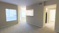Located at 900 Waterford Forest Cir in Cary, NC, this single-floor residence offers a thoughtfully designed open layout that maximizes both space and functionality. The living area is finished with wall-to-wall carpeting in a neutral tone, creating a warm and comfortable atmosphere throughout. Soft, neutral-toned walls complement the light-filled interior, with multiple windows allowing natural light to flow freely into the space.

A standout architectural feature is the pass-through kitchen window, which opens directly into the living area. This design element enhances the sense of openness and connectivity between the kitchen and the main living space, making it ideal for both everyday living and entertaining. The kitchen features a countertop bar ledge at the pass-through, adding a casual dining or workspace option. A pendant light fixture adds a subtle decorative touch above the pass-through opening.

The entryway is conveniently positioned near the living area, with a door that brings in additional natural light. Overhead ventilation fixtures are integrated into the ceiling, contributing to the overall clean and functional design of the space. White trim and baseboards throughout provide crisp contrast against the neutral walls, lending the interior a polished, well-maintained appearance.