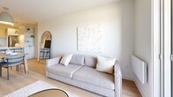 Located at 17 Place de la Triade in Pointe-Claire, Quebec, this well-appointed one-bedroom, one-bathroom unit offers a thoughtfully designed open-concept layout finished in a clean, modern aesthetic throughout. Light hardwood flooring flows seamlessly across the entire living space, complementing the crisp white walls and creating a bright, cohesive atmosphere.

The kitchen is a standout feature, showcasing light wood upper cabinetry, sleek white lower cabinets, a subway tile backsplash, and a peninsula with a white quartz countertop. Stainless steel appliances — including a range, dishwasher, and refrigerator — are paired with pendant lighting, adding a refined, functional touch.

The living room is bathed in natural light from a large sliding glass door that opens onto a private balcony, offering open outdoor views. The bedroom features a generous window framing scenic exterior views, providing a bright and tranquil retreat.

The bathroom is elegantly finished with warm wood-toned cabinetry, a white quartz vanity, large-format floor tiles, and a full bathtub with a glass shower enclosure. A dedicated in-unit laundry area houses a stacked Whirlpool washer and dryer with an overhead storage shelf. A wall-mounted air conditioning unit ensures year-round comfort throughout this stylish, efficiently arranged home.