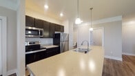 Located at 990 Plumway Ln in Lewis Center, Ohio, this single-floor residence offers a well-designed open-concept layout with modern finishes throughout. The kitchen serves as a central hub, showcasing dark espresso cabinetry, light quartz countertops, stainless steel appliances including a range, built-in microwave, and refrigerator, as well as a peninsula island with an undermount sink and pendant lighting overhead. The kitchen flows seamlessly into the living area, which features rich wood-look flooring, neutral-toned walls, and multiple windows that invite natural light. A dedicated dining or flex space adjoins the main living area, maintaining the open and airy feel of the floor plan. The bedroom features plush carpeting, a generously sized window with blinds, and access to a spacious walk-in closet equipped with wire shelving for organized storage. The bathroom is well-appointed with a sliding glass shower enclosure, a dark-framed vanity mirror, light countertop, and wood-look flooring that ties the space together. Clean white panel doors, recessed lighting, and consistent neutral tones create a cohesive and polished aesthetic throughout this move-in-ready home.