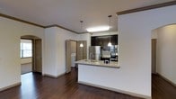 This single-floor residence showcases an open-concept layout that seamlessly connects the living area and kitchen, creating a spacious and functional environment. Rich, dark hardwood flooring extends throughout, providing a warm contrast against the crisp white walls accented with crown molding.

The kitchen is a standout feature, equipped with stainless steel appliances including a refrigerator, microwave, and range. Dark espresso cabinetry provides ample storage and pairs elegantly with the granite countertops. A peninsula with an integrated sink serves as both a functional workspace and a casual dining or entertaining surface. Pendant lighting hangs above the peninsula, adding focused illumination and a stylish touch.

A built-in fluorescent light fixture above the cooking area ensures the kitchen remains well-lit. The open layout allows natural sightlines across the living space, enhancing the sense of openness. Doorways visible in the background lead to additional rooms, including what appears to be a laundry area, suggesting practical in-unit amenities. Overall, the space presents a clean, modern aesthetic with thoughtful design details.