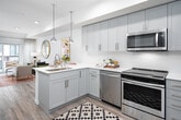 This single-floor residence showcases a thoughtfully designed open-concept layout, where the kitchen flows seamlessly into the living area. The kitchen is outfitted with gray shaker-style cabinetry extending to the ceiling, white quartz countertops, a textured tile backsplash, and a full suite of stainless steel appliances, including a gas range, microwave, dishwasher, and refrigerator. A peninsula with an undermount sink provides additional prep space and accommodates bar seating, illuminated by two pendant lights overhead.

The living area is bright and welcoming, benefiting from natural light streaming through large sliding glass doors that open onto a private balcony. The bedroom is carpeted and generously sized, featuring large windows, a ceiling fan, and ample natural light. It connects directly to a well-equipped bathroom, which includes white shaker cabinetry, quartz countertops, a built-in storage niche, and a shower with a decorative curtain. Wood-look flooring runs throughout the main living areas, and the unit also includes a dedicated laundry space with hookups and built-in shelving.