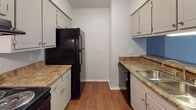 Located at 160 Treetop Dr in Fayetteville, NC, this single-floor residence offers a practical and comfortable layout designed for everyday living. The galley-style kitchen is outfitted with white cabinetry, dark granite-style countertops, a stainless steel sink, and black appliances including a refrigerator, range, and dishwasher, with wood-look flooring running throughout. A pass-through window connects the kitchen to the living area, creating an open, communicative flow between spaces. The living area transitions between wood-look flooring and plush carpet, and features a ceiling fan with light fixture. A sliding glass door leads to a private outdoor balcony, filling the space with natural light and offering views of the surrounding landscape. A half bathroom near the main living area includes a wood-toned vanity with a white countertop and wood-look flooring. The bedrooms are carpeted and bathed in natural light from individual windows, each offering access to dedicated walk-in closets with shelving. The primary bathroom includes a full soaking tub and shower combination, toilet, and wood-look flooring. Throughout, the home maintains a clean, neutral color palette with light gray walls and white trim, providing a bright and move-in-ready environment.