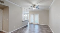 This single-floor residence offers a thoughtfully designed layout that balances comfort and functionality. The open-concept living and dining area is anchored by rich hardwood-style flooring, crown molding, and a ceiling fan, creating a bright and welcoming atmosphere. French doors flood the space with natural light and provide a seamless connection to the outdoors. A kitchen pass-through with pendant lighting bridges the living area to the kitchen, which is outfitted with white shaker-style cabinetry, light stone countertops, a subway tile backsplash, and a full suite of stainless steel appliances, including a refrigerator, range, and built-in microwave. The bedroom features plush carpeting, a ceiling fan with light kit, crown molding, and access to natural light, offering a serene retreat. The bathroom is finished with gray cabinetry, a white countertop vanity, a large mirror, and a tiled shower. Dedicated in-unit laundry adds everyday convenience. Throughout the space, neutral tones, clean lines, and consistent flooring create a cohesive and modern aesthetic that is both practical and inviting.