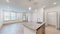 This thoughtfully designed single-floor residence offers 1 bedroom and 2 bathrooms within a efficient, well-organized layout. The open-concept kitchen and living area serves as the heart of the home, anchored by a central granite-topped island with an undermount sink and pendant lighting above. The kitchen features dark taupe cabinetry, stainless steel appliances, and recessed lighting, all flowing seamlessly into the living area, which is brightened by multiple windows and light hardwood-style flooring. A private entry door opens directly into the living space, adding convenience and accessibility. A light-filled hallway connects the main living area to the private quarters, where the bedroom features plush carpeting, natural light from dual windows, and a calm, neutral palette. The en-suite bathroom is well-appointed with granite countertops, a single vanity with taupe cabinetry, a glass-enclosed shower, and direct access to a dedicated walk-in closet with built-in shelving. A second full bathroom and a utility room round out the functional layout. Throughout, clean white walls, consistent light-toned flooring, and recessed lighting create a bright and cohesive living environment.