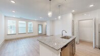 This thoughtfully designed single-floor residence offers 1 bedroom and 2 bathrooms within a efficient, well-organized layout. The open-concept kitchen and living area serves as the heart of the home, anchored by a central granite-topped island with an undermount sink and pendant lighting above. The kitchen features dark taupe cabinetry, stainless steel appliances, and recessed lighting, all flowing seamlessly into the living area, which is brightened by multiple windows and light hardwood-style flooring. A private entry door opens directly into the living space, adding convenience and accessibility. A light-filled hallway connects the main living area to the private quarters, where the bedroom features plush carpeting, natural light from dual windows, and a calm, neutral palette. The en-suite bathroom is well-appointed with granite countertops, a single vanity with taupe cabinetry, a glass-enclosed shower, and direct access to a dedicated walk-in closet with built-in shelving. A second full bathroom and a utility room round out the functional layout. Throughout, clean white walls, consistent light-toned flooring, and recessed lighting create a bright and cohesive living environment.