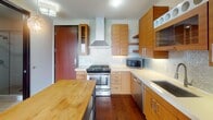 Located in the Lowry Hill East neighborhood of Minneapolis, this two-story residence offers a well-appointed layout spread across two distinct levels connected by a wood-tread staircase. The main level showcases a contemporary kitchen designed with warm bamboo-toned cabinetry, a mosaic tile backsplash, stainless steel appliances including a gas range with a sleek wall-mounted hood, a built-in dishwasher, and a refrigerator with an ice maker. A butcher block island provides additional prep space, while rich hardwood flooring runs throughout the main level. Pendant lighting with decorative globe fixtures adds visual warmth, and large windows allow generous natural light to flow into the adjoining living area, offering views of the surrounding neighborhood. The upper level features carpeted flooring, ceiling fans, and an open loft-style layout bordered by a modern metal railing system that overlooks the lower floor. Windows on the upper level further enhance natural light. A bathroom with large-format tile flooring, a glass-enclosed shower, an integrated vanity with wood cabinetry, and clean neutral finishes completes the space, reinforcing the home's consistent modern aesthetic throughout.