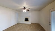 This single-story residence offers two bedrooms and two bathrooms within a generously sized floor plan. The living area serves as the heart of the home, featuring a wood-burning fireplace framed by a brick surround and a raised hearth, creating a focal point that adds warmth and character to the space. A ceiling fan with a built-in light fixture is centrally mounted on the textured, popcorn-style ceiling, providing both airflow and ambient lighting. The floors are covered in neutral-toned carpet, contributing to a cozy atmosphere. Vertical blinds are present, offering privacy and light control. The walls are painted in a clean, neutral white, lending the space a bright and open feel. The overall design reflects a traditional, practical style well-suited for comfortable everyday living. With its classic interior details and functional layout, this residence provides a solid foundation that could easily be personalized to suit a variety of tastes and lifestyles.
