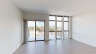 This single-floor unit showcases a clean, contemporary design highlighted by an abundance of natural light. The living area is the standout space, featuring expansive floor-to-ceiling windows and a sliding glass door that opens directly onto a private balcony. The elevated position of the unit affords impressive panoramic views of the surrounding urban skyline, with tree canopy visible in the foreground. Light wood-tone flooring runs throughout, complementing the crisp white walls and adding warmth to the modern aesthetic.

The kitchen is efficiently laid out in a galley-style configuration, equipped with stainless steel appliances including a refrigerator, range, microwave, and dishwasher. Dark wood cabinetry on the lower level contrasts neatly with white upper cabinets, while granite countertops provide a durable and attractive work surface. Recessed lighting illuminates the space, and a barn-style sliding door adds a subtle design detail along the entry corridor.

The bedroom is a well-proportioned, quiet room with wood-tone flooring and a wall-mounted split-system air conditioning unit for individual climate control. The bathroom features a walk-in shower with white tile surround, a granite-topped vanity with under-mount sink, and matching wood-tone flooring, maintaining the unit's cohesive, modern finish throughout.
