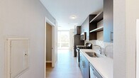 Located at 4901 Broadway in Oakland, CA, this efficient single-floor studio offers a well-planned layout encompassing a combined kitchen and living area, a full bathroom, and a closet. The kitchen is a standout feature, showcasing rich dark-wood cabinetry with sleek hardware, full-height upper cabinets for generous storage, open display shelves, and a decorative geometric tile backsplash. A complete suite of stainless steel appliances — including a gas range, microwave, refrigerator, and dishwasher — is complemented by clean white countertops and a single-basin sink, making the kitchen both functional and visually refined. Light wood-tone flooring runs throughout the space, lending warmth and visual continuity. The living area benefits from a large floor-to-ceiling window that floods the room with natural light and offers views of surrounding Oakland greenery and the neighborhood streetscape. The bathroom features large-format light tile flooring, a vanity with storage, and a clean, neutral color palette. Neutral gray walls throughout the unit provide a versatile backdrop. The overall design aesthetic is modern and minimalist, with thoughtful attention to detail and quality finishes that maximize the utility and comfort of this compact, contemporary Oakland residence.