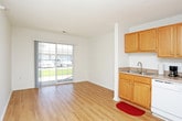 This single-floor space offers a practical and straightforward layout designed for comfortable everyday living. The living area is generously proportioned, featuring light wood-style laminate flooring and crisp white walls that create a clean, open feel. A large sliding glass door floods the space with natural light and provides a view of the surrounding greenery, enhancing the sense of openness. A textured ceiling runs throughout the main living areas, adding a subtle design element consistent across the unit.

The kitchen is efficiently arranged in an L-shaped configuration, outfitted with warm honey-toned wood cabinetry offering ample upper and lower storage. White appliances, including a range, dishwasher, and full-size refrigerator, are neatly integrated alongside a single-basin sink. The kitchen continues the light laminate flooring, maintaining visual cohesion with the living space.

The bedroom is carpeted in a neutral tan tone, providing a softer underfoot feel. A window fitted with horizontal blinds allows natural light while maintaining privacy. The full bathroom includes a shower-tub combination, a toilet, and a vanity with a stone-look countertop, all finished with light wood flooring and clean white fixtures throughout.