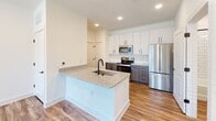 Located at 336 Chestnut Pkwy in Indian Trail, NC, this single-floor home offers a clean, contemporary design with thoughtful finishes throughout. The kitchen serves as the centerpiece of the space, showcasing a large island with a granite countertop and an undermount sink with a matte black faucet. White upper cabinetry is paired with charcoal gray lower cabinets, creating a striking two-tone contrast complemented by a classic subway tile backsplash. Stainless steel appliances, including a French door refrigerator, electric range, and microwave, complete the modern kitchen ensemble. Warm hardwood-style flooring flows through the kitchen and main living areas, adding continuity and a welcoming feel. Recessed lighting and crisp white walls keep the space bright and open. The bathroom is well-appointed with a granite vanity top, an undermount sink, a matte black faucet, and a tiled shower-tub combination featuring white subway tile and matte black fixtures. A bedroom with plush neutral carpet, white walls, and a window with blinds offering views of the surrounding neighborhood rounds out this well-designed home, providing a comfortable and move-in-ready living environment.