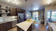 This single-floor residence showcases a thoughtfully designed open-concept layout that seamlessly connects the kitchen, dining, and living areas. The kitchen is outfitted with dark walnut cabinetry, white quartz countertops, a subway tile backsplash, and a full suite of stainless steel appliances, including a French door refrigerator, range, microwave, and dishwasher. A large island with pendant lighting provides additional prep space and casual seating. Open shelving adds both function and visual interest.

The living area flows naturally from the kitchen and is anchored by light hardwood-style flooring, a patterned area rug, and a sliding glass door that opens to a private balcony, allowing ample natural light. The bedroom features a tray ceiling with a ceiling fan, a large window with outdoor views, bold geometric accent wallpaper, and generous space for furnishings. A second bedroom or den is also present, offering flexibility.

The bathroom includes a wood-vanity with a white basin, subway tile tub surround, and herringbone-patterned accent walls. An in-unit stacked washer and dryer is conveniently located nearby. Throughout, a cohesive yellow and grey palette ties the residence together with a modern, vibrant aesthetic.