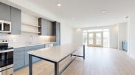 Located at 117 N Oak St in Wichita, Kansas, this modern single-floor residence offers four bedrooms and one bathroom across a thoughtfully designed layout. The open-concept kitchen and living area serves as the heart of the home, featuring sleek gray cabinetry, a white subway tile backsplash, stainless steel appliances, and a large island with a white countertop and steel-framed base. Light wood-look flooring runs throughout the main living areas, enhancing the bright, airy atmosphere created by recessed lighting and large windows. The living room opens to a balcony through glass French doors, inviting abundant natural light and outdoor views. Built-in shelving and a blue accent cabinet add functional character to the living space. The four bedrooms are carpeted and well-proportioned, with the primary bedroom offering generous space. Ceiling fans are installed throughout the bedrooms, adding comfort. The bathroom is finished with large-format tile flooring, a floating gray vanity, and clean white walls, maintaining the home's modern aesthetic. Two closets provide additional storage. The overall design reflects a clean, contemporary style with a cohesive neutral palette accented by slate blue cabinetry details.