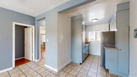 Located on S Ridgeley Drive in Los Angeles, CA, this single-floor, 2-bedroom, 1-bathroom residence offers a practical and efficient layout. The interior is finished with a cool blue-gray color palette throughout, creating a cohesive and calming ambiance across all rooms.

The galley-style kitchen is a standout feature, lined on both sides with tall, light blue cabinetry that maximizes vertical storage. Stainless steel appliances complement the cabinetry, while tile flooring and a window at the far end bring in natural light. The kitchen connects directly to the living area and hallway, facilitating easy flow throughout the unit.

Both bedrooms feature warm hardwood flooring and ceiling fans, contributing to a comfortable living environment. The primary bedroom includes mirrored sliding closet doors with built-in shelving and overhead storage cabinets, enhancing both storage capacity and the sense of space. Windows with blinds allow for natural light and privacy control. A wall-mounted air conditioning unit is also present in the bedrooms for climate control.

The bathroom is clean and bright, featuring a white tub-shower combination with a handheld showerhead, a single vanity with a mirror cabinet, and a small window for ventilation. The all-white finish gives the bathroom a crisp, functional appearance.

A connecting hallway ties all rooms together, making navigation intuitive within this efficiently designed home.