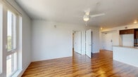 This thoughtfully designed one-bedroom, one-bathroom unit offers a modern and functional layout spread across a single floor. Warm hardwood-style flooring runs throughout, providing visual continuity across all rooms and complementing the clean, white walls and contemporary finishes.

The open-concept kitchen and living area serves as the heart of the unit. The kitchen is well-equipped with dark wood cabinetry, stainless steel appliances including a range and over-the-range microwave, and a central island with a built-in sink and neutral countertops — ideal for both cooking and casual dining. The adjacent living area is bright and open, benefiting from large floor-to-ceiling windows and a glass door leading to a private balcony, offering direct views of the surrounding urban streetscape.

The bedroom is a comfortable, well-proportioned retreat featuring a ceiling fan with light fixture, a large window that invites natural light and outdoor views, and access to a closet. The full bathroom is finished with dark wood cabinetry, a wide vanity with a light countertop, a large mirror, and matching hardwood-style flooring. Additional spaces include a hallway, closet, and dedicated entrance, contributing to practical, everyday living. The unit combines modern aesthetics with functional design throughout.