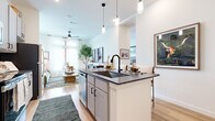 Located on Roy Rd in Denton, TX, this well-appointed one-bedroom, one-bathroom residence offers a smart, efficient layout with stylish modern finishes. The open-concept kitchen and living area forms the heart of the home, anchored by a central island with dark granite countertops, an undermount sink with a matte black faucet, and pendant lighting overhead. Gray shaker-style cabinetry, subway tile backsplash, and stainless steel appliances complete the kitchen. The adjacent living room is bathed in natural light from floor-to-ceiling windows dressed with sheer white curtains, creating an airy, bright atmosphere with light hardwood flooring throughout. The bedroom offers plush carpeting, generous wall space, and tall windows that frame outdoor views, providing a calm and restful retreat. The full bathroom features classic white subway tile surrounding the soaking tub and shower, a gray vanity with granite countertops, and warm hardwood-style flooring. A spacious walk-in closet with built-in shelving and hanging rods provides excellent storage. Completing the layout is a dedicated in-unit laundry room equipped with a full-sized washer and dryer, adding everyday convenience to this well-rounded residence.