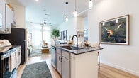 Located on Roy Rd in Denton, TX, this well-appointed one-bedroom, one-bathroom residence offers a smart, efficient layout with stylish modern finishes. The open-concept kitchen and living area forms the heart of the home, anchored by a central island with dark granite countertops, an undermount sink with a matte black faucet, and pendant lighting overhead. Gray shaker-style cabinetry, subway tile backsplash, and stainless steel appliances complete the kitchen. The adjacent living room is bathed in natural light from floor-to-ceiling windows dressed with sheer white curtains, creating an airy, bright atmosphere with light hardwood flooring throughout. The bedroom offers plush carpeting, generous wall space, and tall windows that frame outdoor views, providing a calm and restful retreat. The full bathroom features classic white subway tile surrounding the soaking tub and shower, a gray vanity with granite countertops, and warm hardwood-style flooring. A spacious walk-in closet with built-in shelving and hanging rods provides excellent storage. Completing the layout is a dedicated in-unit laundry room equipped with a full-sized washer and dryer, adding everyday convenience to this well-rounded residence.