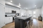 This well-appointed one-bedroom, one-bathroom unit in Meridian, Idaho offers a thoughtfully designed layout with a clean, modern aesthetic. Light hardwood flooring runs throughout the space, complementing the bright white walls and contemporary finishes that create a cohesive, airy atmosphere.

The kitchen is a standout feature, centered around a large island with a quartz countertop, undermount sink, and integrated dishwasher. Stainless steel appliances — including a refrigerator, range, and built-in microwave — pair with white cabinetry, a tiled backsplash, and pendant lighting to deliver both style and function. An adjacent pantry provides valuable additional storage.

The living area flows naturally toward a private balcony, accessible through a glass-panel door that invites natural light into the space and offers outdoor views of the surrounding neighborhood.

The bedroom is comfortably sized with large windows that frame outdoor greenery, filling the room with natural light. A dedicated closet adds practical storage.

The bathroom features a floating white vanity with a dark quartz countertop, an undermount sink, and a backlit mirror, all set against light hardwood flooring. An in-unit laundry area with a stacked Bosch washer and dryer rounds out the functional amenities of this modern residence.