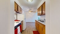 This single-floor, one-bedroom, one-bathroom unit offers a practical and efficiently organized layout. The galley-style kitchen is the functional centerpiece, featuring warm wood cabinetry lining both walls, a stainless steel sink, a electric range, and a full-size refrigerator. Light wood-look flooring runs throughout the kitchen, which opens directly into the living area via a wide doorway. A ceiling fan is positioned at the transition point between the kitchen and living space, providing air circulation across both areas.

The living room is carpeted and receives natural light through a wide set of windows fitted with horizontal blinds, offering views of surrounding trees. A wall-mounted air conditioning unit and baseboard heater provide year-round climate control. The space is open and adaptable for various furniture arrangements.

The bedroom is also carpeted and features a generously sized walk-in closet with built-in shelving and a hanging rod, offering substantial storage capacity. A window allows natural light into the room, and a baseboard heater is positioned along the wall.

The bathroom includes a full-size tub and shower combo enclosed with white ceramic tile, a toilet, and tile flooring, providing a clean and functional design. A hallway connects all rooms, contributing to an organized and straightforward floor plan throughout the unit.