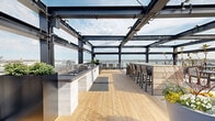 This expansive rooftop terrace in Baltimore's 21230 zip code delivers a sophisticated outdoor amenity space defined by contemporary industrial design and panoramic views. A bold steel pergola framework spans much of the terrace, providing partial overhead coverage while remaining open to natural light and sky views. The structure accommodates string lighting and built-in systems, creating ambiance for both daytime and evening use.

The terrace is organized into several distinct functional zones. A fully equipped outdoor kitchen features a built-in grill, sink, and marble-clad cabinetry, positioned to take advantage of waterfront sightlines. Multiple bar seating areas are distributed across the space, including a long perimeter counter with bar stools overlooking the cityscape, a central wood-clad communal high-top table, and additional seating nodes throughout.

Underfoot, warm-toned wood deck planking and large-format stone pavers define different zones across the terrace. Lush planting beds, oversized decorative planters filled with seasonal flowers and greenery, and slatted wood privacy screens add softness and texture to the industrial aesthetic. A quiet seating nook with a teak bench is nestled among garden plantings. Sweeping views of Baltimore's harbor and skyline complete the setting.