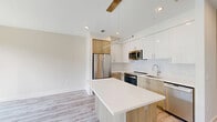 Located at 925 S Glebe Road in Arlington, VA, this thoughtfully designed one-bedroom, two-bathroom unit offers a clean, modern aesthetic with high-quality finishes throughout its efficiently utilized floor plan. Light-toned luxury vinyl plank flooring flows seamlessly from room to room, complementing the bright white walls and recessed lighting that keep the space feeling open and airy.

The contemporary kitchen serves as a central highlight, featuring a large island with a crisp white quartz countertop, a dual-tone cabinetry scheme combining white upper cabinets with warm wood-finish lower cabinets, a subway tile backsplash, and a full suite of stainless steel appliances. Pendant lighting with gold accents adds a refined touch overhead. A stacked washer and dryer unit is conveniently integrated into the kitchen area.

The bedroom offers a comfortable footprint with large windows that invite ample natural light and views of the surrounding neighborhood. A dedicated closet provides practical storage.

Both bathrooms are finished with large-format neutral tile and sleek modern fixtures. The primary bath features a glass-enclosed walk-in shower with floor-to-ceiling tile and a wood-accented vanity with an undermount sink. The hallway leading through the unit is clean and well-proportioned, with multiple doors providing access to the closet and secondary bathroom.