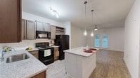 This thoughtfully designed 2-bedroom, 1-bathroom home offers a practical and modern layout across a single floor. The open-concept kitchen and living area serves as the heart of the home, featuring rich dark-stained cabinetry, granite countertops, a classic white subway tile backsplash, and black appliances including a range, microwave, and dishwasher. A central kitchen island with a granite top and pendant lighting above adds both workspace and a casual dining option. Light wood-look flooring runs throughout the common areas, while the living space benefits from natural light and access to the outdoors via French doors, complemented by a ceiling fan overhead.

The two bedrooms are carpeted for comfort, each receiving natural light through windows with blinds. The primary bedroom is generously sized and features a ceiling fan, along with access to a walk-in closet outfitted with extensive wire shelving for organized storage. The shared bathroom is well-equipped with a dual-sink granite vanity, wood-look tile flooring, and a shower-tub combination. Additional highlights include multiple closets throughout, a dedicated laundry area, and a connecting hallway that ties the layout together efficiently. The home combines practical functionality with clean, contemporary finishes.