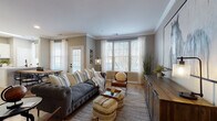This single-floor residence offers a thoughtfully designed layout that balances comfort and modern style. The living area is a standout space, featuring crown molding, warm hardwood-style flooring, and generous windows dressed with sheer white curtains that allow abundant natural light to fill the room. The space accommodates a tufted gray sofa, a leather accent chair, and a wooden media console, creating an inviting and cohesive atmosphere.

The kitchen is outfitted with crisp white shaker-style cabinetry, a classic subway tile backsplash, light quartz countertops, and a full suite of stainless steel appliances including a gas range, built-in microwave, and refrigerator. A peninsula with an undermount sink adds both function and additional workspace.

The residence includes two bedrooms, each carpeted and finished with neutral tones that promote a calm, restful environment. Both rooms feature windows with sheer curtains and ample space for full-sized furnishings. The bathroom is finished with white cabinetry, quartz countertops, matte black hardware, a soaking tub with tiled surround, and direct access to a spacious walk-in closet. Throughout the residence, a cohesive neutral palette and modern farmhouse-inspired design elements create a warm and functional living environment.