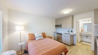 Located at 2070 McMillan Ave in North Charleston, SC, this thoughtfully designed studio offers a smart, efficient layout that maximizes every square foot. The main living area seamlessly integrates sleeping and kitchen functions, featuring light wood-tone cabinetry, stainless steel appliances including a microwave and dishwasher, and a granite-topped kitchenette with a sink — all set against clean white walls and warm wood-look flooring that runs throughout the space. A large window allows natural light to fill the room, creating a bright and open ambiance. The space is served by two bathrooms: one features a full soaking tub with a shower combination and a decorative curtain, finished in crisp white; the second functions as a vanity area with an expansive granite countertop, an undermount sink, built-in open shelving, and warm wood-look flooring — offering ample preparation and storage space. Together, these two bathrooms provide notable convenience for a studio of this scale. The overall design aesthetic is clean and contemporary, with neutral tones and modern fixtures that create a cohesive, comfortable living environment suited for efficient urban living in North Charleston.
