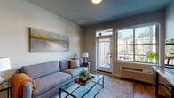 This single-floor residence at 13470 SE 162nd Ave in Happy Valley, Oregon, offers a well-designed open-concept layout that seamlessly connects the main living areas. The living room is a welcoming space featuring warm-toned hardwood-style flooring, a glass-top coffee table, and a large exterior door with transom window above, allowing ample natural light and outdoor views of the surrounding neighborhood.

The kitchen is appointed with dark espresso cabinetry reaching toward the ceiling, stainless steel appliances including a refrigerator, range, and built-in microwave, and granite countertops. A peninsula with bar seating and pendant lighting above separates the kitchen from the dining and living areas, creating a functional and social hub. An adjacent pantry provides additional storage.

The bedrooms feature plush carpeting and generously sized windows that bring in natural light and neighborhood views. The bathroom includes a full soaking tub with shower combination finished in clean white surroundings with wood-look flooring. Throughout the residence, neutral gray walls and consistent flooring create a cohesive, contemporary aesthetic well-suited to everyday living.