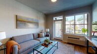 This single-floor residence at 13470 SE 162nd Ave in Happy Valley, Oregon, offers a well-designed open-concept layout that seamlessly connects the main living areas. The living room is a welcoming space featuring warm-toned hardwood-style flooring, a glass-top coffee table, and a large exterior door with transom window above, allowing ample natural light and outdoor views of the surrounding neighborhood.

The kitchen is appointed with dark espresso cabinetry reaching toward the ceiling, stainless steel appliances including a refrigerator, range, and built-in microwave, and granite countertops. A peninsula with bar seating and pendant lighting above separates the kitchen from the dining and living areas, creating a functional and social hub. An adjacent pantry provides additional storage.

The bedrooms feature plush carpeting and generously sized windows that bring in natural light and neighborhood views. The bathroom includes a full soaking tub with shower combination finished in clean white surroundings with wood-look flooring. Throughout the residence, neutral gray walls and consistent flooring create a cohesive, contemporary aesthetic well-suited to everyday living.