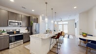 This thoughtfully designed one-bedroom, two-bathroom home offers a smart and functional layout across a single floor. The open-concept kitchen serves as the centerpiece, featuring a large granite-topped island with an integrated sink and seating for multiple bar stools, dark espresso cabinetry, a classic white subway tile backsplash, stainless steel appliances, and elegant teardrop pendant lighting overhead. Wood-look flooring extends throughout the main living areas, seamlessly connecting the kitchen to the bright and airy living room. The living room benefits from abundant natural light through large windows and a glass-paned door that opens onto a private balcony, with a ceiling fan adding comfort overhead. The primary bedroom is a serene retreat, carpeted for warmth, with a ceiling fan and a natural light-filled window. It connects to a spacious en-suite bathroom complete with a dual-sink granite vanity, dark cabinetry, and wood-look flooring, and provides access to a generously sized walk-in closet with multi-level shelving and hanging rods. A dedicated office with carpet flooring, dual windows, and a ceiling fan offers a quiet workspace. Two closets provide ample storage throughout the home, rounding out a well-organized and comfortable living environment.