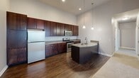 This well-appointed 2-bedroom, 1-bathroom unit in Valparaiso, Indiana offers a thoughtfully designed single-floor layout. The kitchen is a standout, featuring dark espresso cabinetry reaching to the ceiling, granite countertops, stainless steel appliances, and a curved island with pendant lighting and hardwood-style flooring. The full bathroom includes a granite vanity, dark cabinetry, and a tub-shower combination. Both bedrooms are carpeted with neutral tones and offer ample natural light. The primary bedroom includes a walk-in closet with wire shelving. A private balcony with exposed wood beam accents provides scenic views of the surrounding community and greenery.