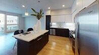 Located at 1000 Elements Way in Irvine, CA, this modern single-floor residence offers a well-designed layout with contemporary finishes throughout. The open-concept kitchen is a standout feature, showcasing two-tone cabinetry with dark lower cabinets and crisp white upper cabinets, stainless steel appliances including a gas range, microwave, refrigerator, and dishwasher, and a large center island with a white quartz countertop and bar seating beneath stylish pendant lighting. Recessed lighting and wood-look flooring throughout the main living areas contribute to a bright, cohesive aesthetic. The living area extends seamlessly from the kitchen and opens to a private balcony through a glass door, allowing for an abundance of natural light and outdoor access. The bedroom features plush carpeting, a ceiling fan, and a spacious walk-in closet outfitted with wire shelving and hanging rods for ample storage. An in-unit washer and dryer are conveniently located nearby. The bathroom is appointed with a dual-sink vanity featuring dark cabinetry, white quartz countertops, and large mirrors with sleek modern lighting, complemented by louvered closet doors and wood-look flooring. Clean lines, neutral tones, and quality finishes define the overall ambiance of this well-appointed Irvine residence.