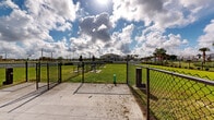 Located at 2507 Koji St in Mount Dora, Florida, this single-level outdoor property offers a generously sized, well-maintained green space set within a residential community. The lot is characterized by its expansive, neatly kept lawn that stretches across the entirety of the property, providing an open and versatile outdoor environment.

The perimeter is defined by a combination of white vinyl privacy fencing and black wrought-iron and chain-link fencing, creating a clear boundary while maintaining a clean, orderly aesthetic. Landscaped plantings along the fence lines add visual interest and a touch of greenery to the borders. A concrete pad area is visible on one side of the lot, along with what appear to be utility access points, suggesting infrastructure readiness.

The property enjoys wide-open views of the surrounding Mount Dora community, with neighboring single-story homes, tall palm trees, and magnolia trees visible in the distance. A seating bench is positioned along one section of the perimeter, offering a functional outdoor rest area. Street-level lighting poles are present, indicating illumination for evening use.

Under the famously bright Florida sky, the lot benefits from abundant natural light throughout the day. The overall setting reflects a well-kept, community-oriented environment with ample open space suitable for a variety of outdoor uses.