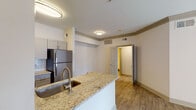 This single-floor space is designed with a clean, contemporary aesthetic that emphasizes an open and functional layout. Light wood-style flooring flows consistently throughout, creating a cohesive and airy feel across all rooms.

The living area is generously proportioned, featuring crown molding, a ceiling fan, and a bank of French doors fitted with blinds that allow natural light to filter in while offering views to the outdoors. The front entryway opens directly into this space, providing a welcoming and accessible flow.

The kitchen is designed as a peninsula layout, anchored by granite countertops with an integrated sink and a full suite of stainless steel appliances, including a refrigerator, range, and microwave. Gray shaker-style cabinetry lines the walls above a white subway tile backsplash, and a walk-in pantry or utility closet is accessible directly from the kitchen.

The bedrooms are bright and neutrally finished, each with wood-style flooring, windows with blinds, and ceiling fans for comfort. One bedroom features access to a walk-in closet.

The bathroom is outfitted with a wide vanity, a large frameless mirror, globe lighting, and a walk-in shower, maintaining the clean, practical character found throughout the space.