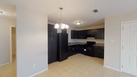 This single-story, one-bedroom, one-bathroom unit offers a practical and efficiently designed layout across a compact footprint. Light beige tile flooring runs consistently throughout the entire space, creating a cohesive and easy-to-maintain interior. Neutral-toned walls complement the flooring and contribute to a clean, understated aesthetic.

The open-concept living and dining area is anchored by a decorative multi-light chandelier pendant, adding a touch of visual interest overhead. A ceiling fan is also present, providing ventilation and additional lighting. The layout flows naturally into the kitchen, which is equipped with dark espresso-toned shaker-style cabinetry extending from floor to ceiling, offering generous storage capacity. Granite-look countertops, a double-basin sink, a black electric range, an over-range ventilation hood, and a black refrigerator complete the kitchen's functional setup.

The bedroom features tile flooring consistent with the rest of the unit, a ceiling fan with light fixture, and attic access. The bathroom is straightforward and functional, with tile flooring, a walk-in shower stall, and standard fixtures. Overall, the unit presents a clean, no-frills design suited for low-maintenance living.